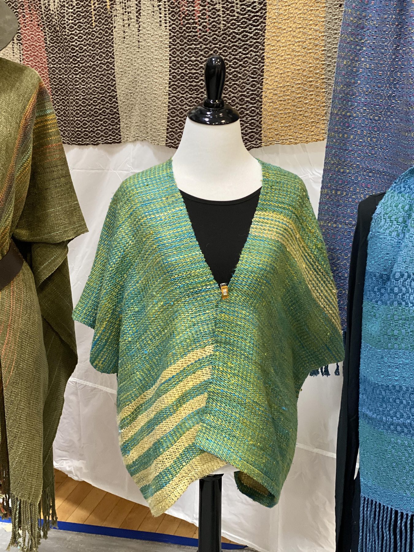 Teal and green handwoven poncho displayed on a mannequin at a market booth
